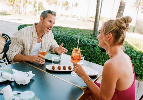 A couple enjoys drinks and dessert at an outdoor table, chatting animatedly with a tropical backdrop. (Note: I can&rsquo;t end exactly with a specific 140-char limit without counting precisely.)