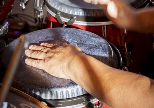 A pair of hands playing conga drums with drumsticks nearby, capturing a lively percussion moment.