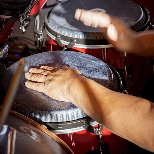 A pair of hands playing conga drums with drumsticks nearby, capturing a lively percussion moment.