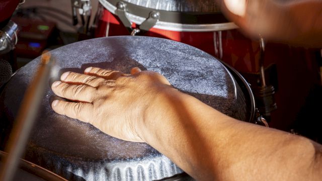 A pair of hands playing conga drums with drumsticks nearby, capturing a lively percussion moment.