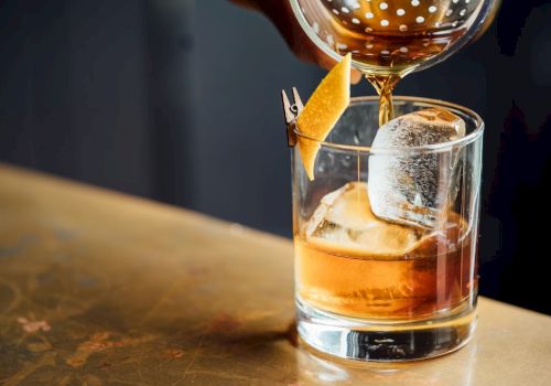 A whiskey on the rocks being poured with a citrus twist garnish in a short glass.