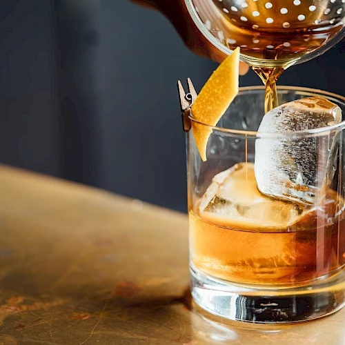 A whiskey on the rocks being poured with a citrus twist garnish in a short glass.