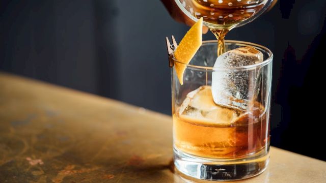 A whiskey on the rocks being poured with a citrus twist garnish in a short glass.