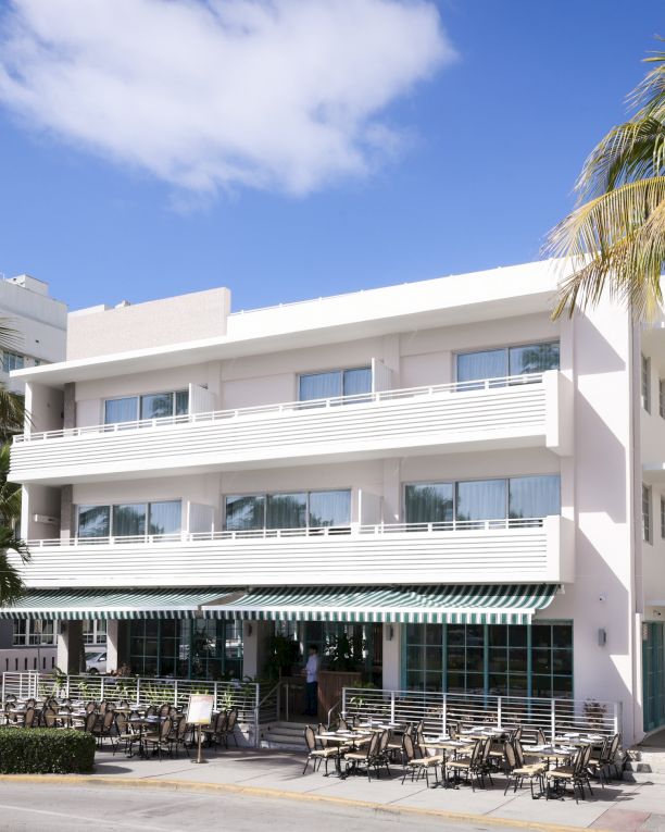 A sunny beachfront hotel with white balconies, palm trees, and outdoor seating ready for guests. Top it at 140 characters, always ending the sentence.