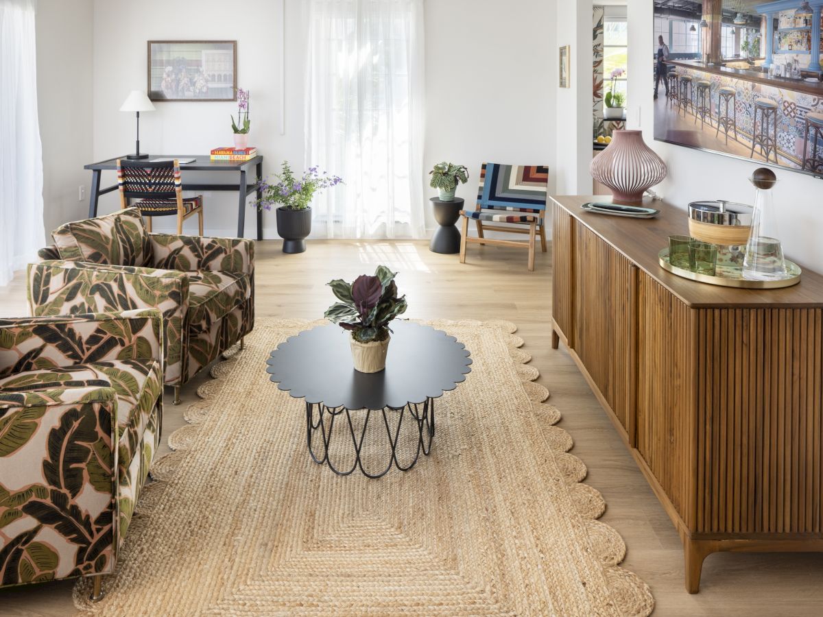 A bright, mid-century living room with floral-patterned sofas, a woven rug, a round coffee table, and a wooden sideboard along the wall.