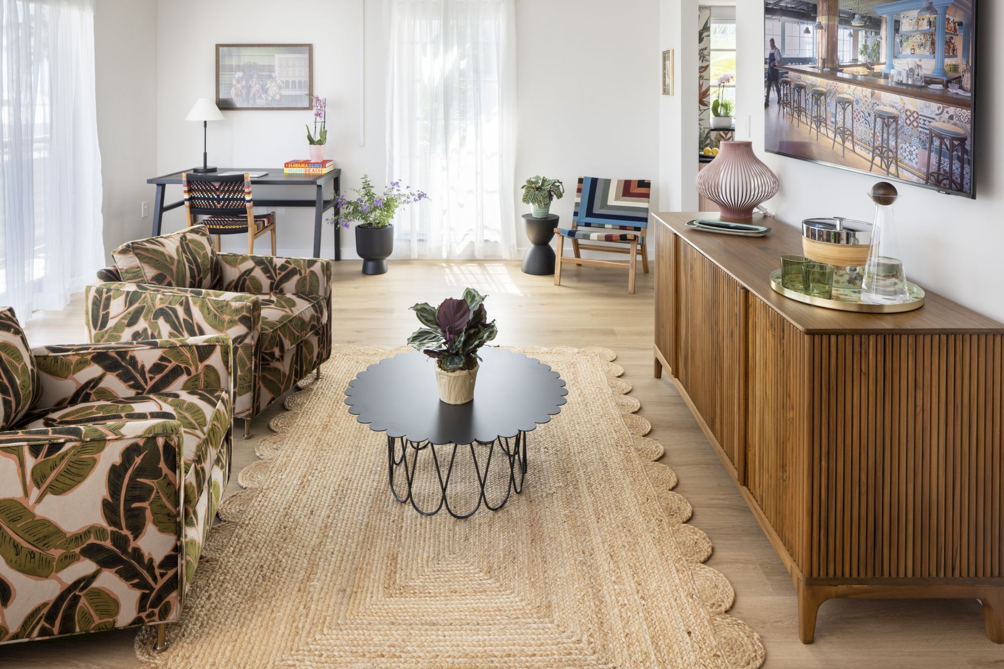 A bright, mid-century living room with patterned sofas, a woven rug, a round coffee table, and a wooden sideboard against the wall.