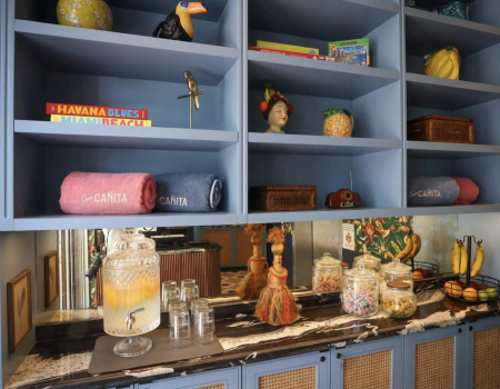 A colorful cabinet with blue shelves holding decorations, plants, books, and figural items; a marble counter displays glass jars, bottles, and snacks. End.
