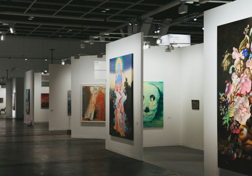 A modern art gallery with tall white partitions displaying colorful paintings on both sides, subdued lighting, and a spacious interior.