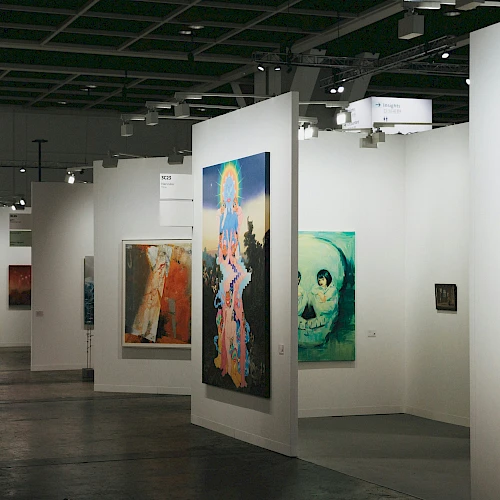A modern art gallery with tall white partitions displaying colorful paintings on both sides, subdued lighting, and a spacious interior.