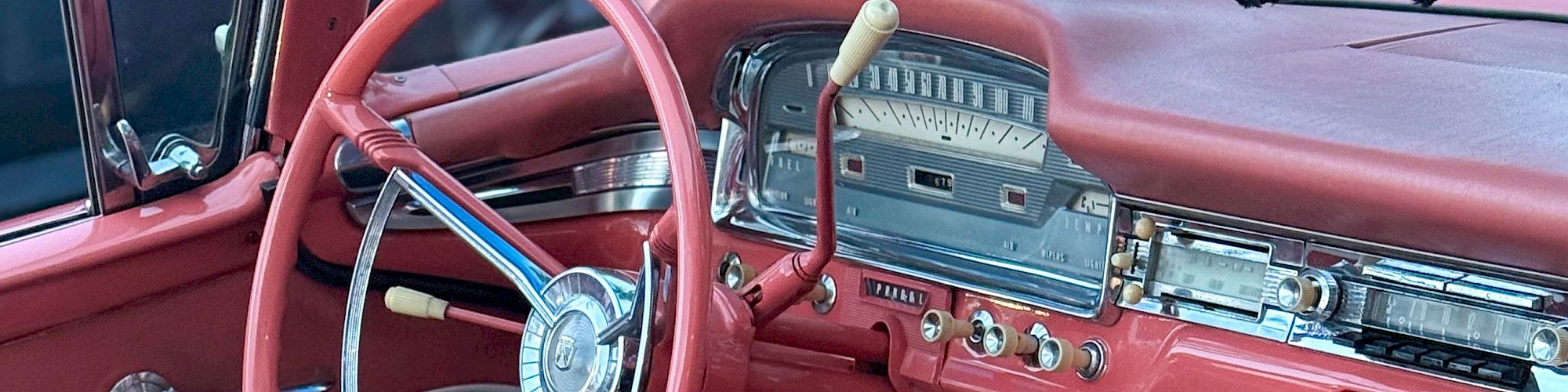 A classic red vintage car interior with a chrome dashboard, pink steering wheel, and checkered seat covers, exuding retro charm.