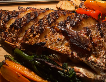 Grilled ribeye steak with char marks, roasted carrots and peppers, and greens on a wooden board, juicy, sizzling, and perfectly seasoned.