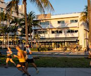 A sunny hotel courtyard with palm trees, outdoor seating, and people blurred by motion walking past.