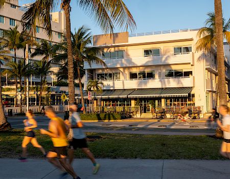 A sunny hotel courtyard with palm trees, outdoor seating, and people blurred by motion walking past.